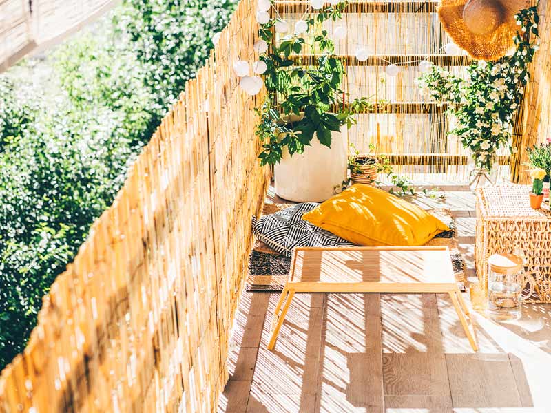 Small apartment balcony furniture idea with mat & small wooden table - Beautiful Homes