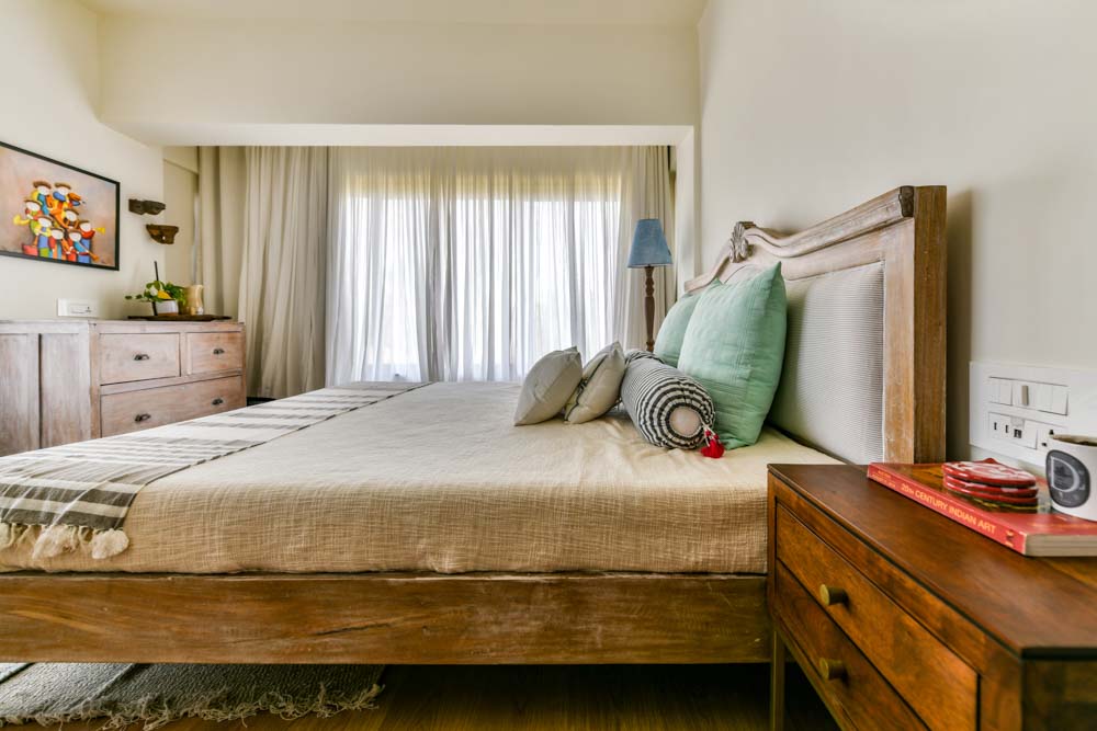 Bedroom décor is done with soft white walls & sheer curtains with pop bright cushions - Beautiful Homes