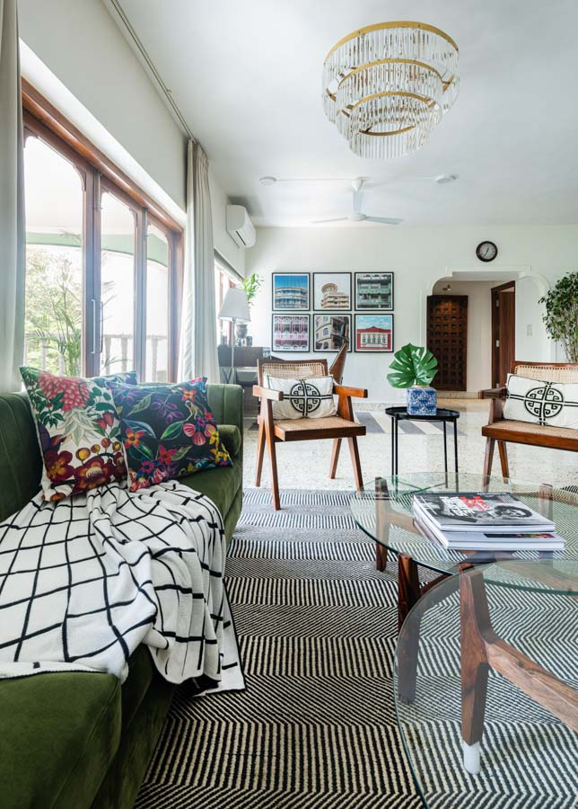Green sofa with striped throw and wooden furniture in bright living room with big window, framed photographs on wall