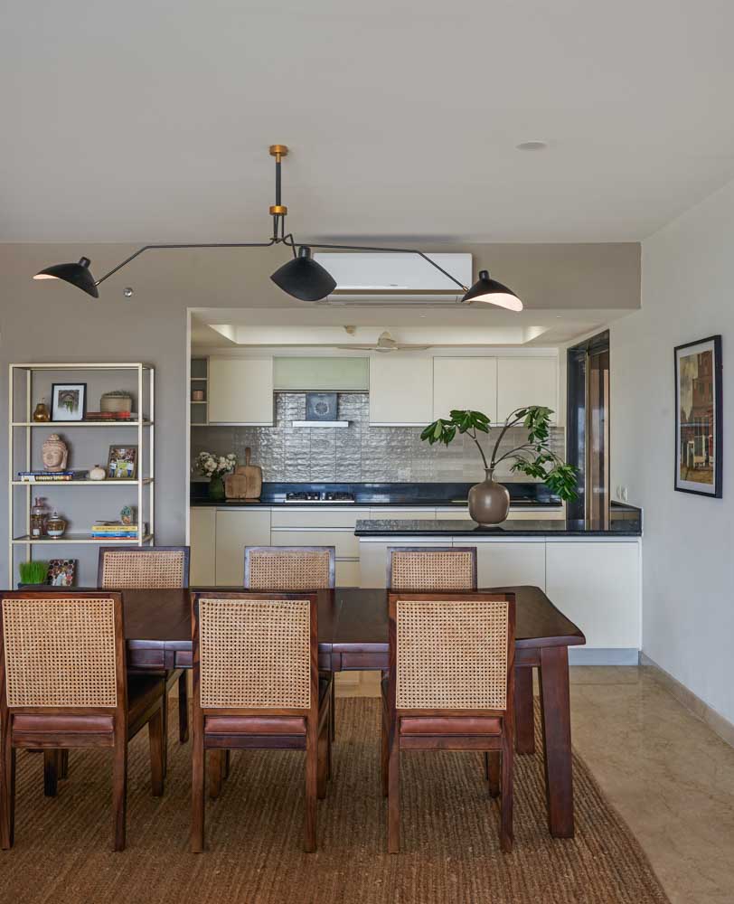 A six seater dining table with rattan chairs and behind it is a kitchen