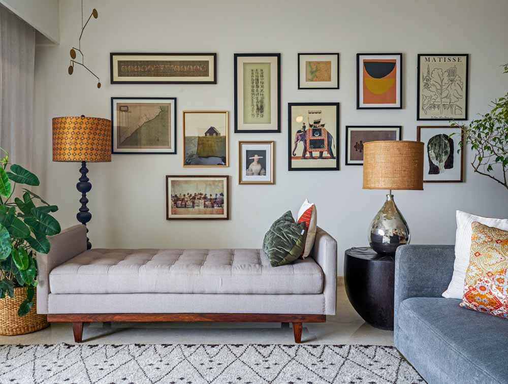 A gallery wall filled with frames and in front of it is. agrey bench