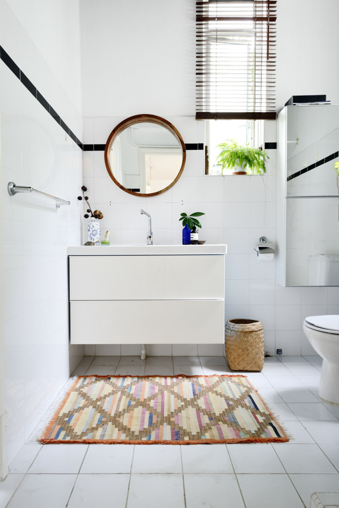 Small and white bathroom with accessories such us wicker waste basket, potted plants and no-fuss mirrors