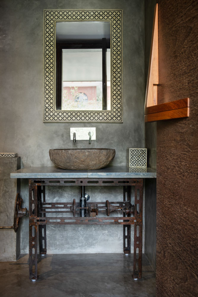 Dark bathroom with accessories such as ornate mirror and stone wash basin on steampunk piece of iron