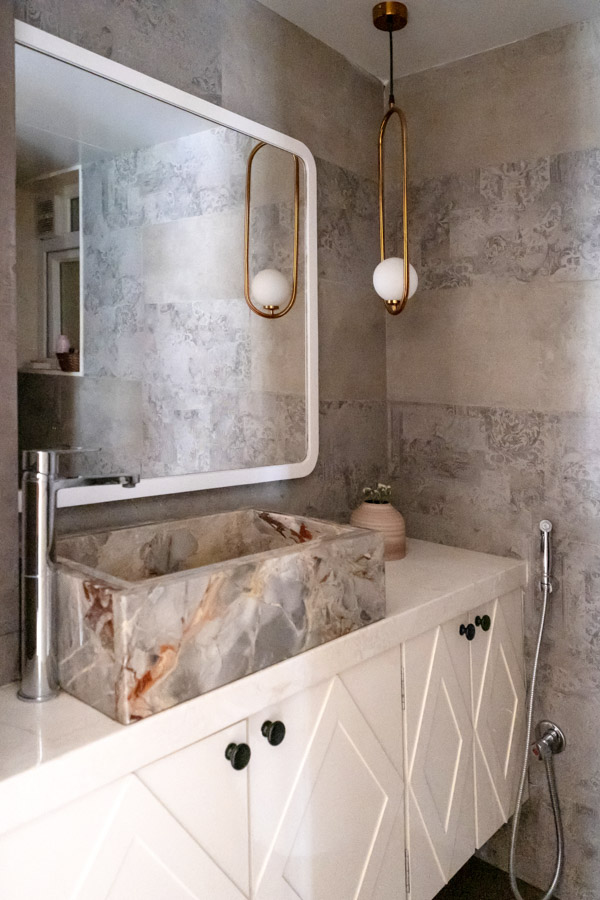 Single golden bathroom light hanging in a bathroom mostly in stone with earthy hues
