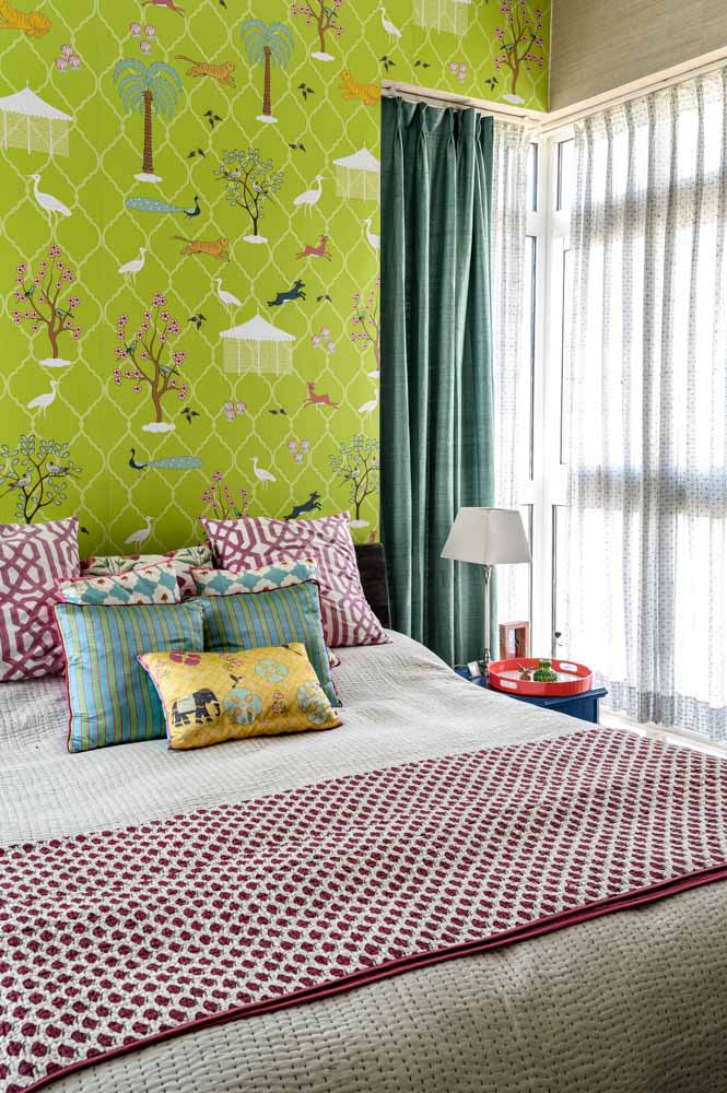 Wallpaper for bedroom in lush green with playful motifs of flora and fauna, bed with many colourful cushions - Beautiful Homes