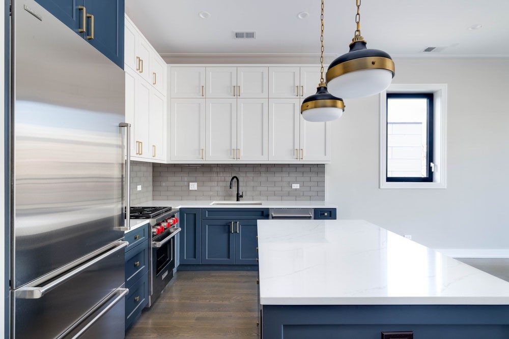 A neat & clean modular kitchen with tiled wall, pendant lights & cabinets of the colour blue & white - Beautiful Homes