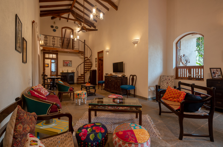 Ethnic family room with colourful cushions and ottoman, wooden ceiling and twisted staircase