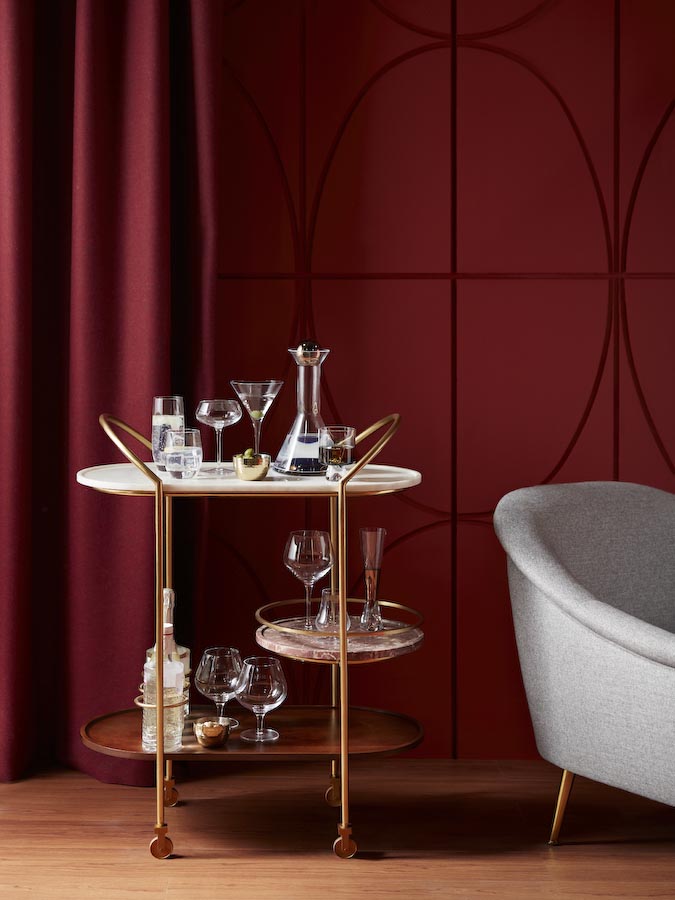 Home Bar Design With Bar Trolley In Wood, Metal & Marble Holding Liquor & Cocktail Glasses On A Deep Purple Wall- Beautiful Homes