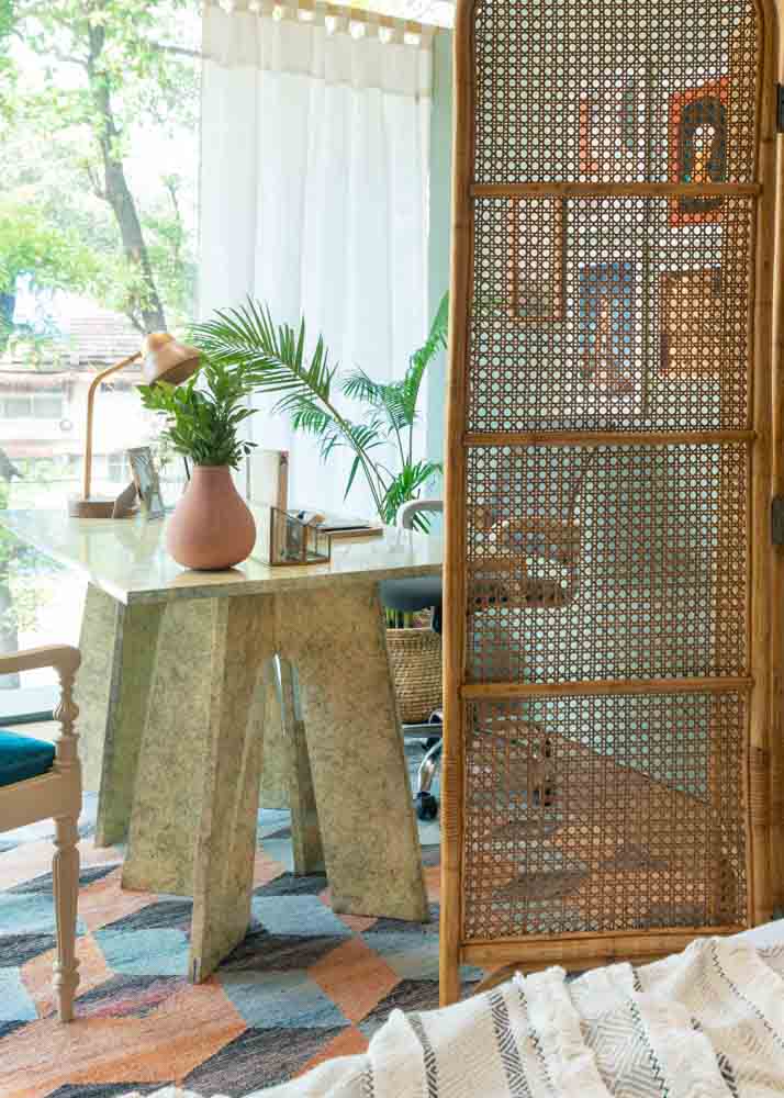 A study table placed on a rug, with a pink flower vase placed on the table and a rattan room divider besides the table