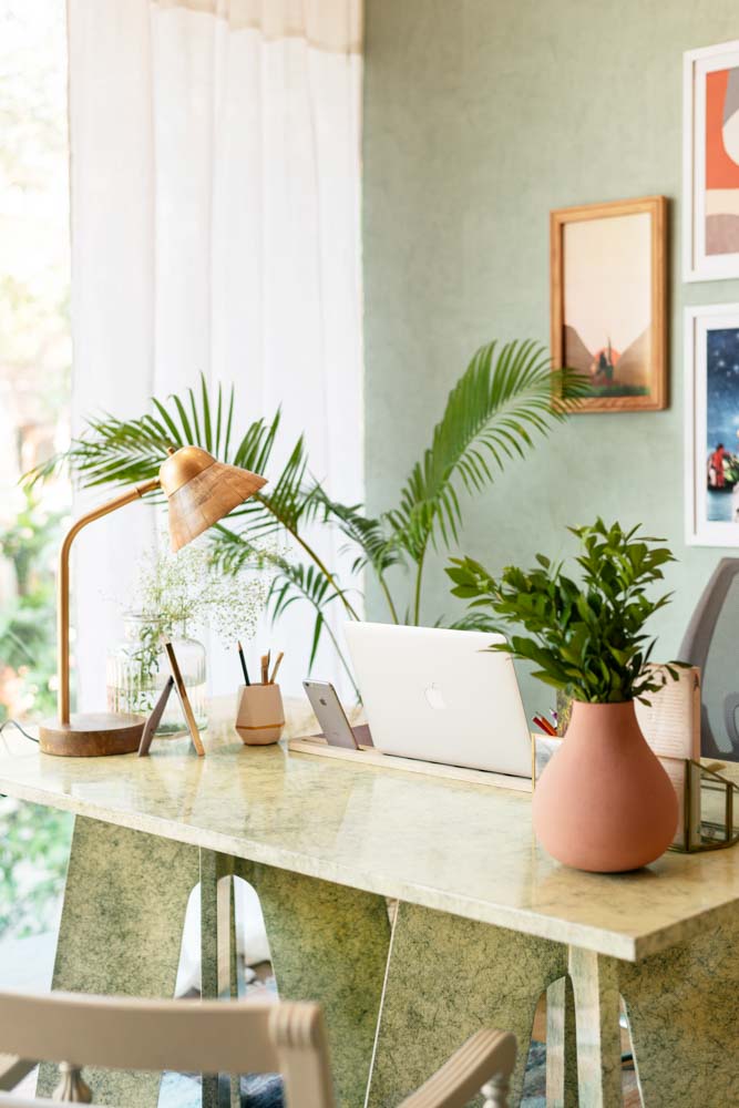 A study table with a laptop, a table lamp and a pink flower vase
