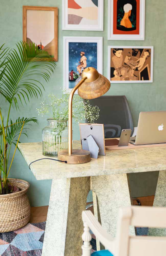 A wooden lamp placed on a study table, a photo frame, a laptop and a planter besides the table
